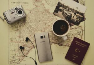 Camera, phone, headphones, Turkish passport, and cup of black coffee on top of a black and white map 