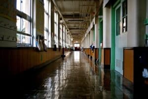 Empty school hallway with polished floors, large windows, and classroom doors lining the corridor.